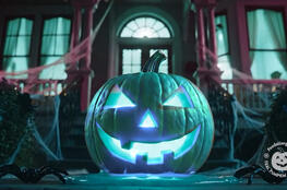 Teal Pumpkin Jack-o-Lantern with spooky lighting in front of a house at night.