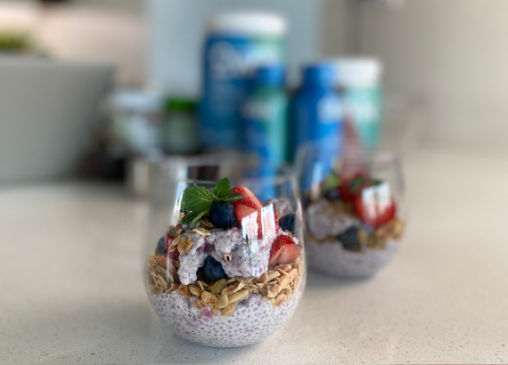 A parfait in a glass with blurred OWYN products in the background.
