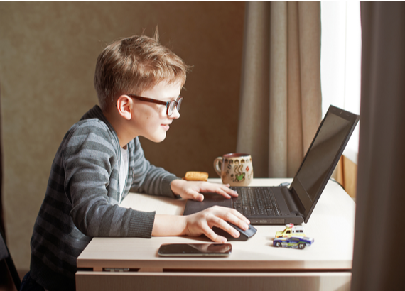 Young boy wearing glasses, at a desk talking to friends on a computer