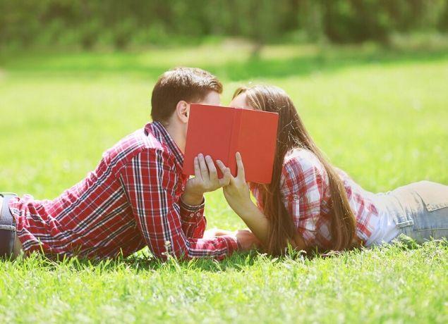Teens kissing behind book