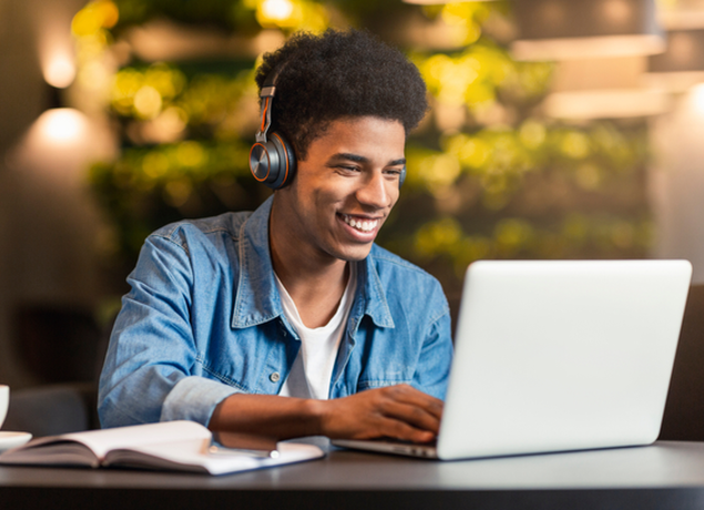 College boy on computer wearing headphones and smiling