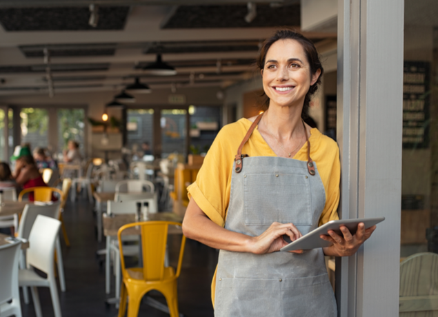 Woman standing outside restaurant with apron and ipad