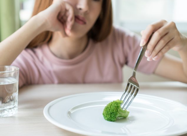 girl pushing a piece of broccoli around her plate