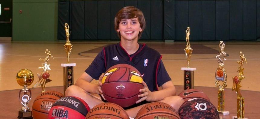 Kid sitting with a lot of basketballs and trophies 